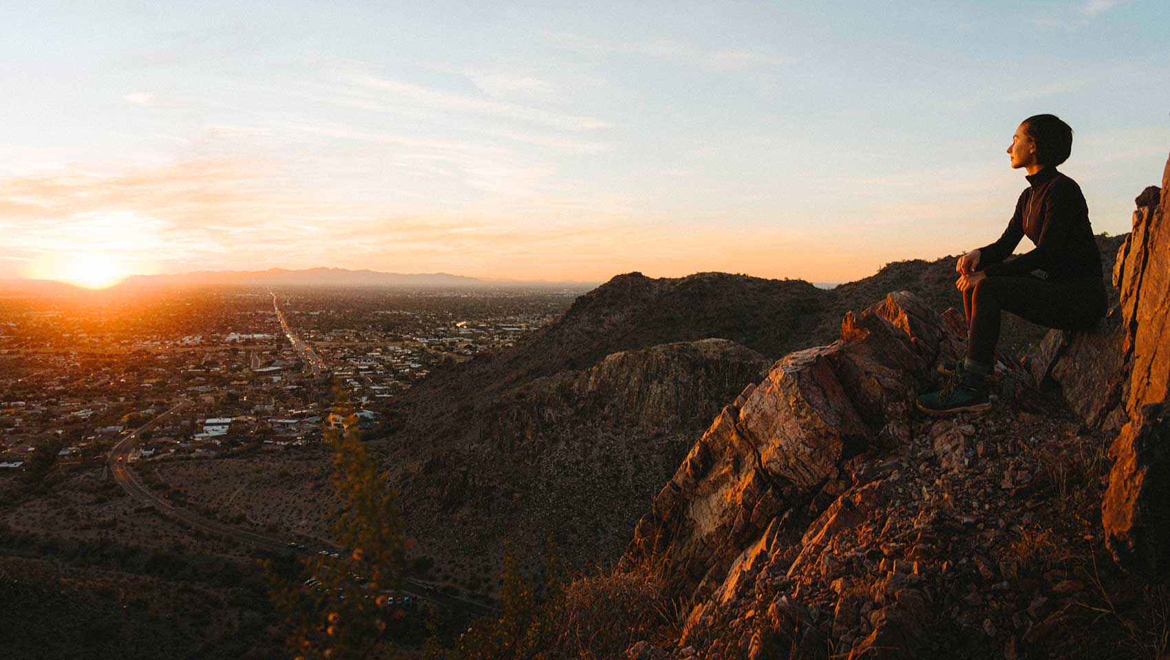Woman sitting on rocky mountain overlooking sunrise