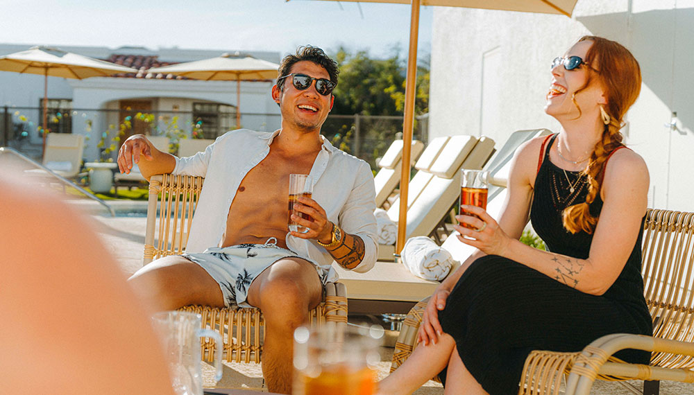 Man and woman laughing with drinks poolside at Kimpton Miralina