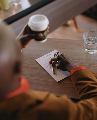 person at meeting with coffee, water, pad and pen