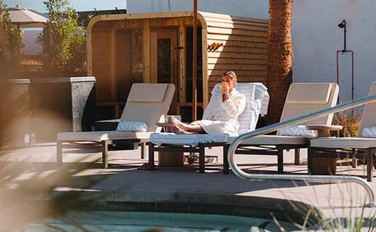 Woman sips a drink while sitting on a lounge chair by the Miralina pool under an umbrella
