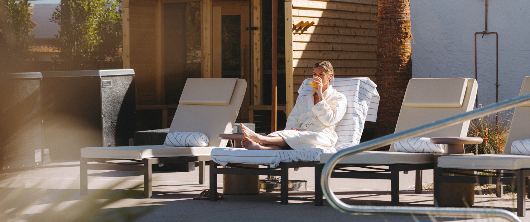 woman on chaise lounge by the Kimpton miralina resort pool sippy in a drink and wearing a white robe